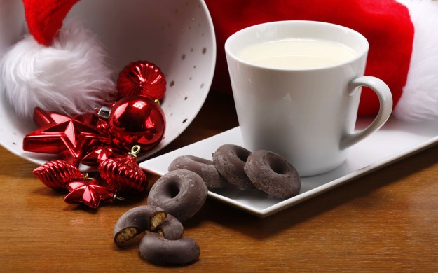 glass of milk with small donut shaped cookies and Christmas decorations on a table