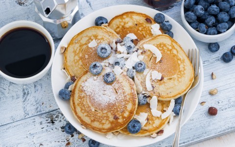plate of blueberry pancakes and black coffee