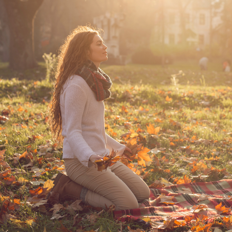 Woman kneeling on a grass filed covered with orange leaves