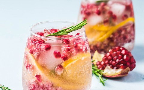 Two cranberry and orange cocktails garnished with rosemary  