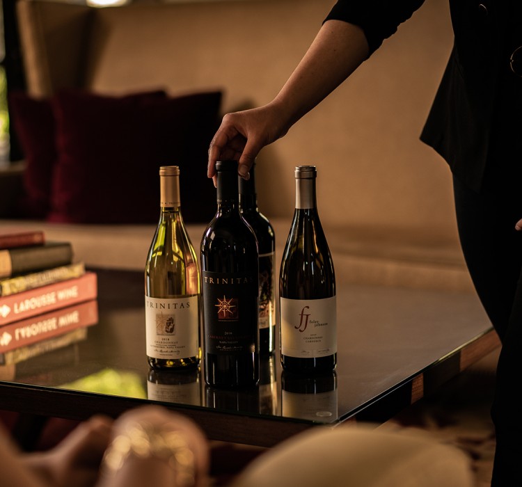 close up of a meritage employee showcasing a selection of wine bottles for a guest
