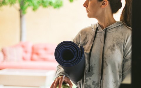 Woman holding a yoga mat and a green juice 