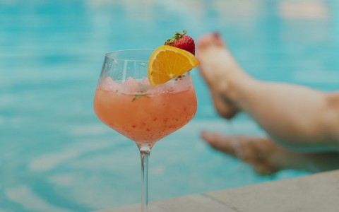 Woman sitting pool side with a pink frozen cocktail