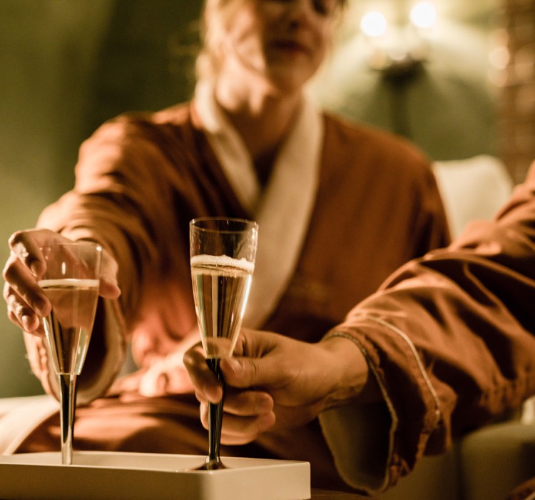 man and woman in robes toasting champagne while they relax at the spa