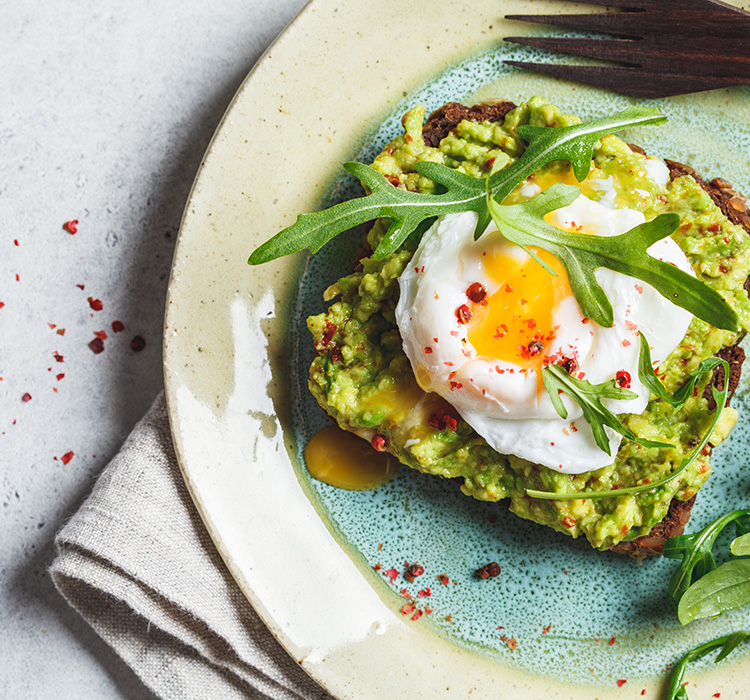 overhead view of avacado toast with sunny-side up egg served on a plate