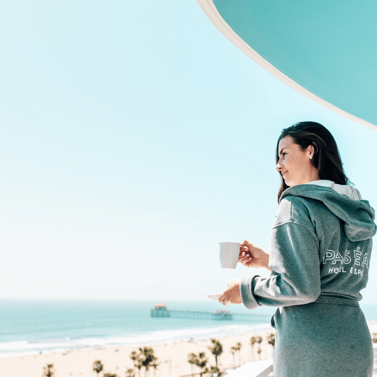 Woman in a robe having coffee while looking at the ocean