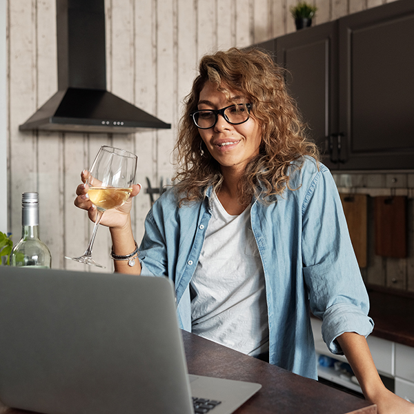 Woman holding a glass of white wine while looking at her computer