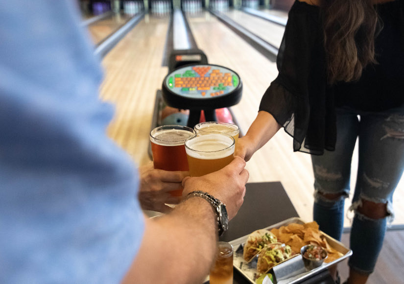 Friends in a bowling alley cheering with beer glasses