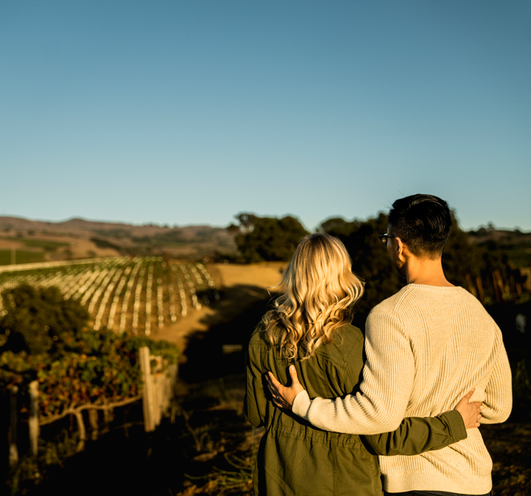 man and woman couple standing arm in arm looking out over the meritage vineyards