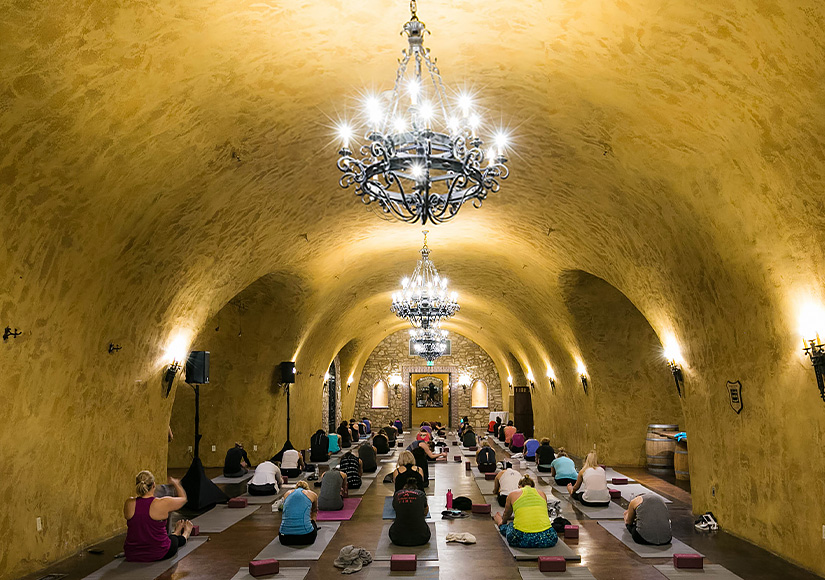 Full yoga class with people stretching in a long tunnel space decorated with chaneliers