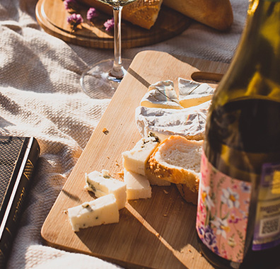 cheese board with a selection of cheeses and bread at a picnic with a bottle of wine