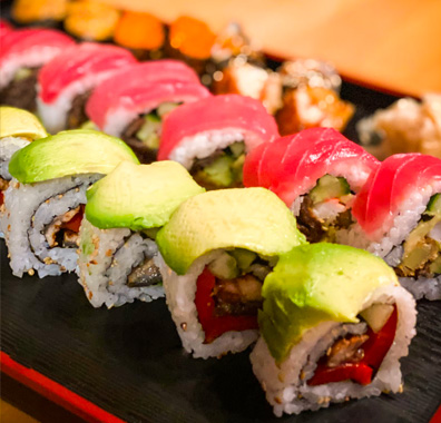close up view of fresh sushi rolls topped with avacado and another with salmon sashimi
