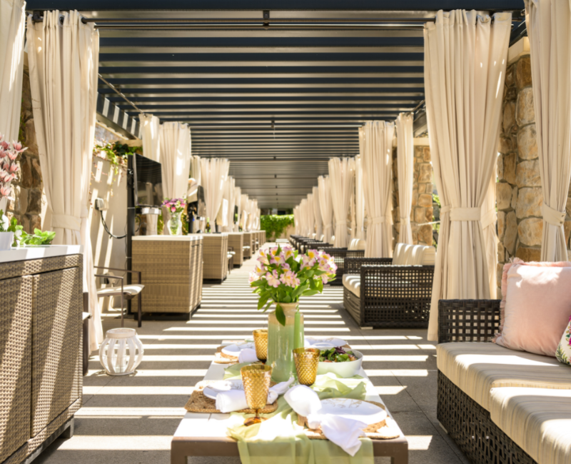 View of several pool cabanas with sofas and a set up table