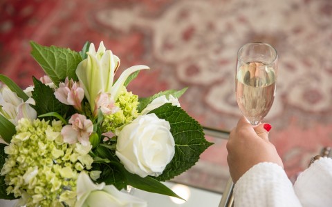 view of a woman hand holding a glass of champagne next to a flower arrangement