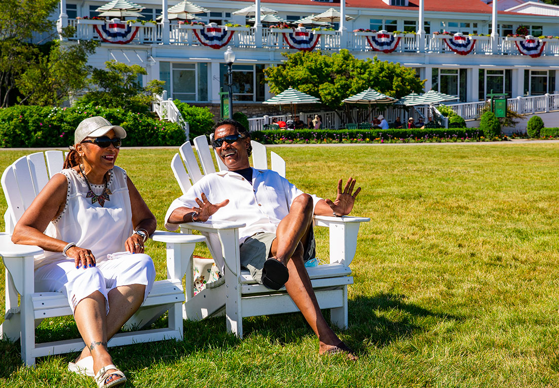 man and woman smiling outside while sitting on white chairs