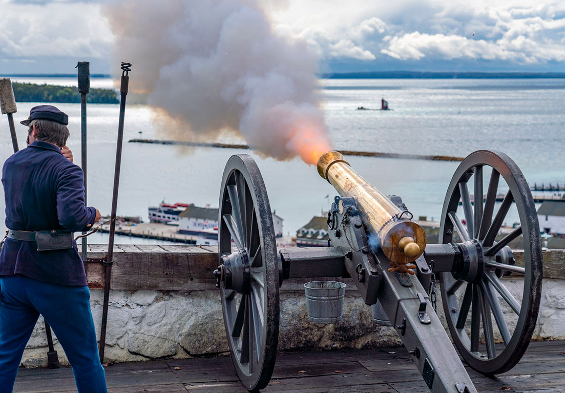 a man dressed in a blue uniform standing next to a battery wager as it shoots towards the ocean