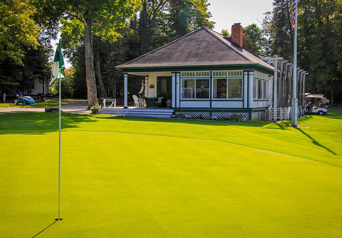 club golf course club house facing the golf course with the golf carts on the side of the club house and the a golf pole a few feet away from of the club house