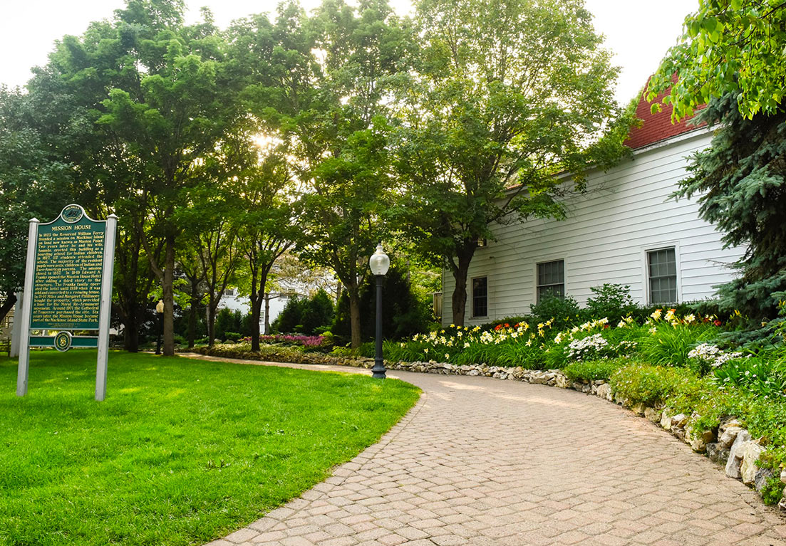 outside area with, side walk, trees, grass and a green sign with yellow writing .