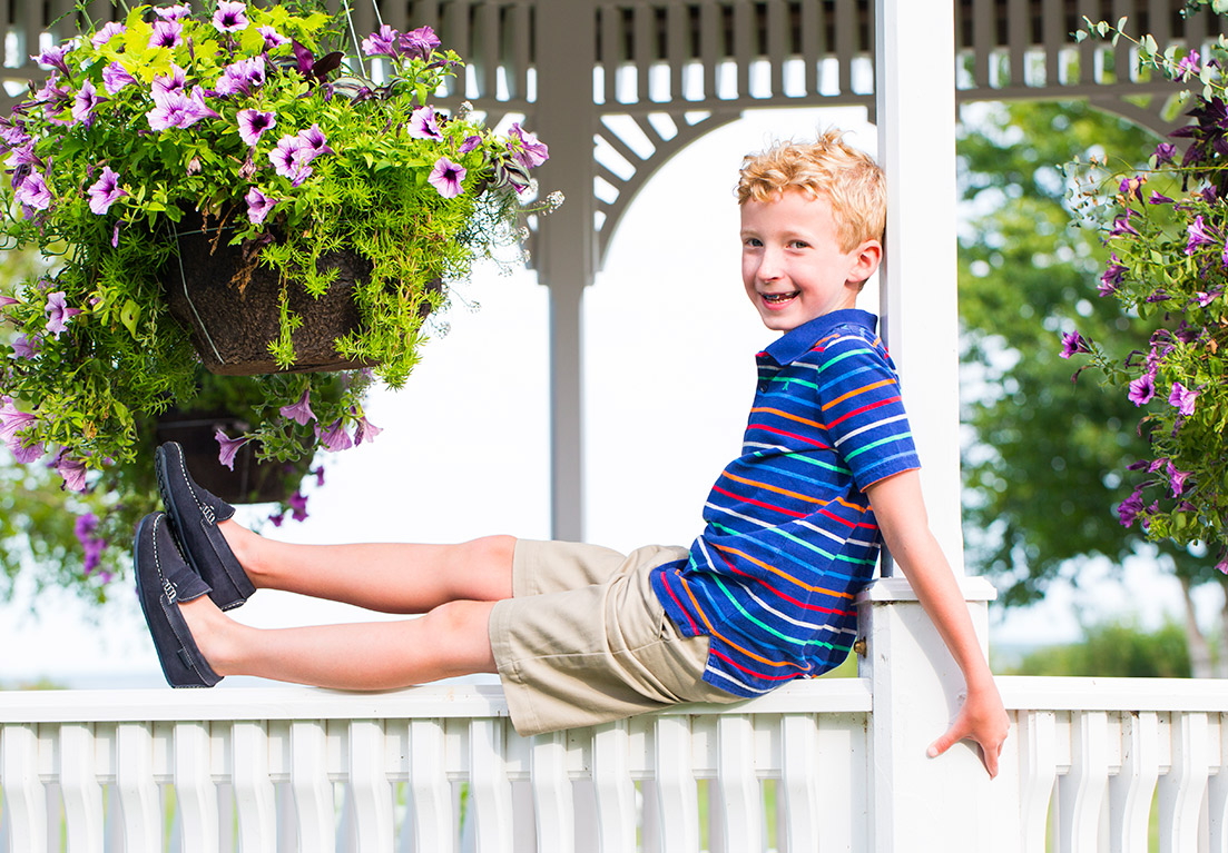 a little boy sitting on railing of a gazebo while while putting is back on the post and holding on to the post