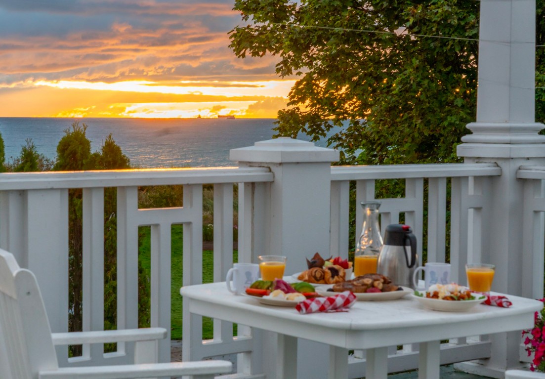 white table set up with breakfast plates and orange juice and coffee in front of the sunrise on the water