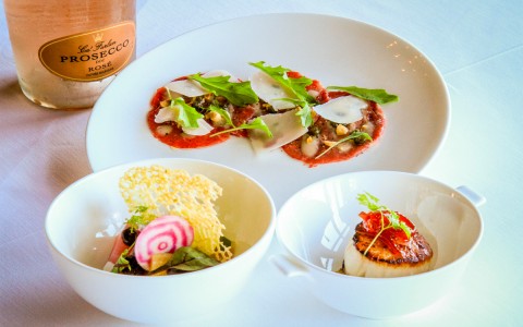 decorative food dishes on white plates with a bottle of rose prosecco in the back
