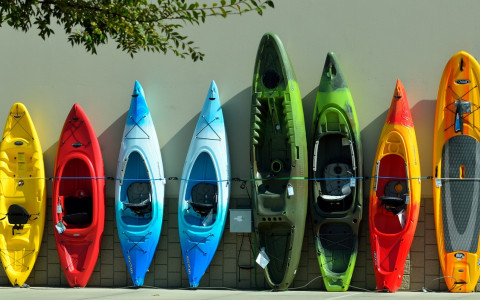 Eight kayaks of different colors propped against a wall