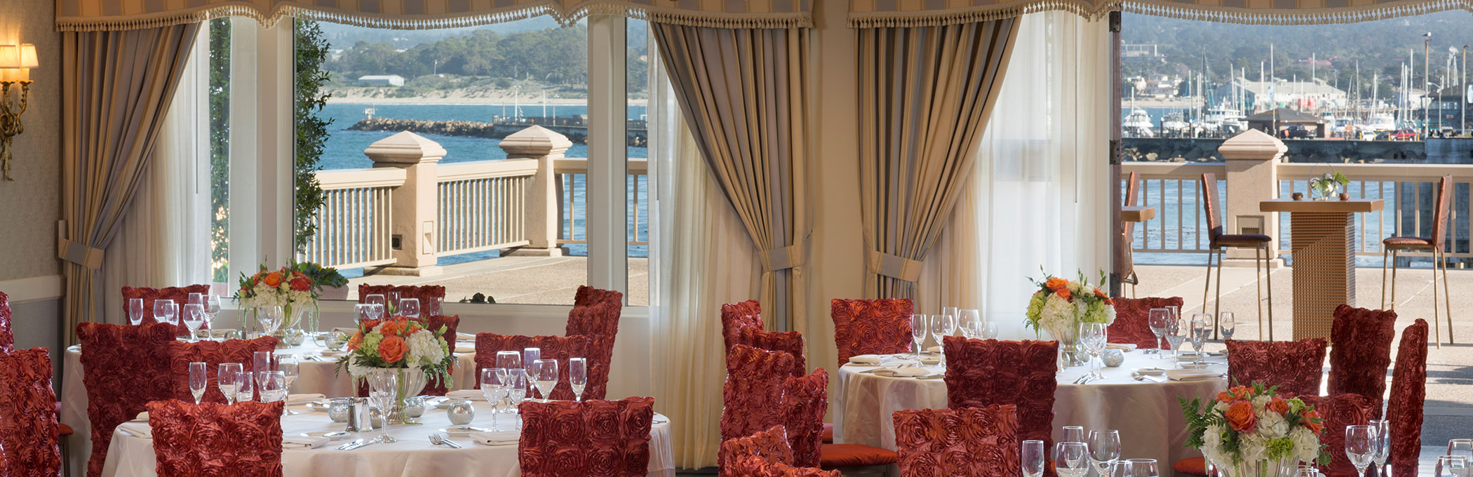 event space set with round tables and red chairs looking out to the patio and ocean view