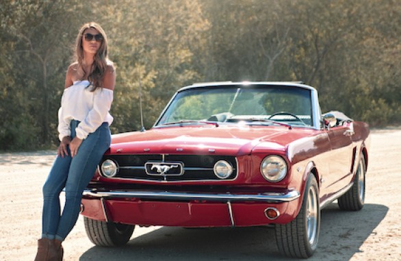 Woman sitting on a old red mustang convertible