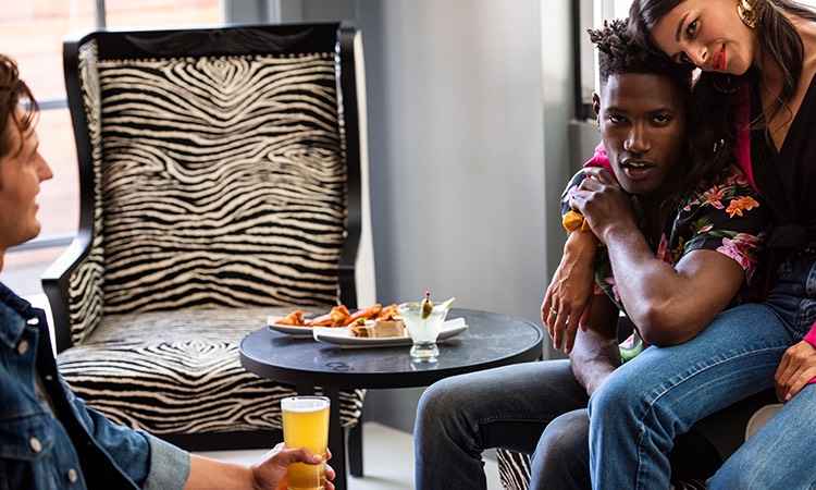 Three friends sitting in zebra striped chairs drinking beer and cocktails