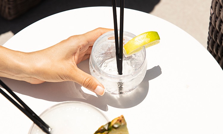 A Hand holding a cocktail with 2 black straws in the sunlight