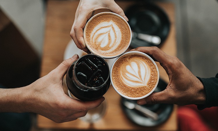 Three hands each holding a beverage toasting each other