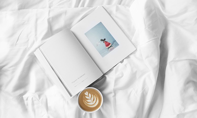 Cup of espresso on a bed with white linens and open book