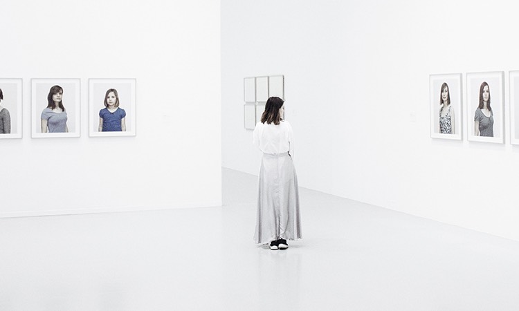 Woman walking around a stark white museum with portraits on the walls