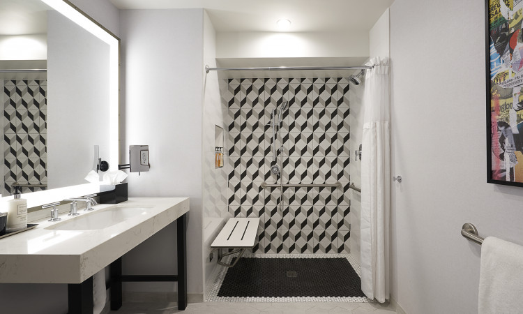 ADA bathroom with a black and white tiled shower with an ADA seat and grab bars