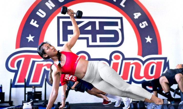 woman in red sports bra and white leggings holding side plank with dumbell in raised arm