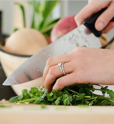 womans hands cutting up herbs on a wooden cutting board