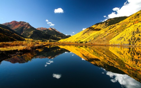 a smooth lake with big green and yellow colored mountains all around it during the day