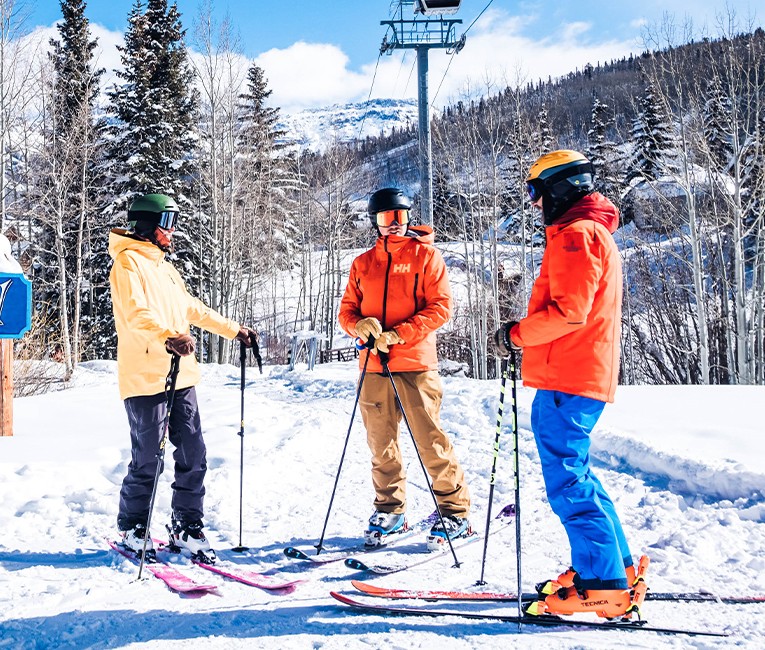 three skiers gathered in a small circle outside during the day with snow covered mountains in the distance