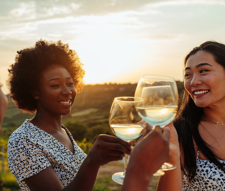 close up of women holding their glasses of white wine as the sun sets in the distance