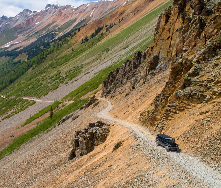 a black truck driving along a rocky road next to a mountain