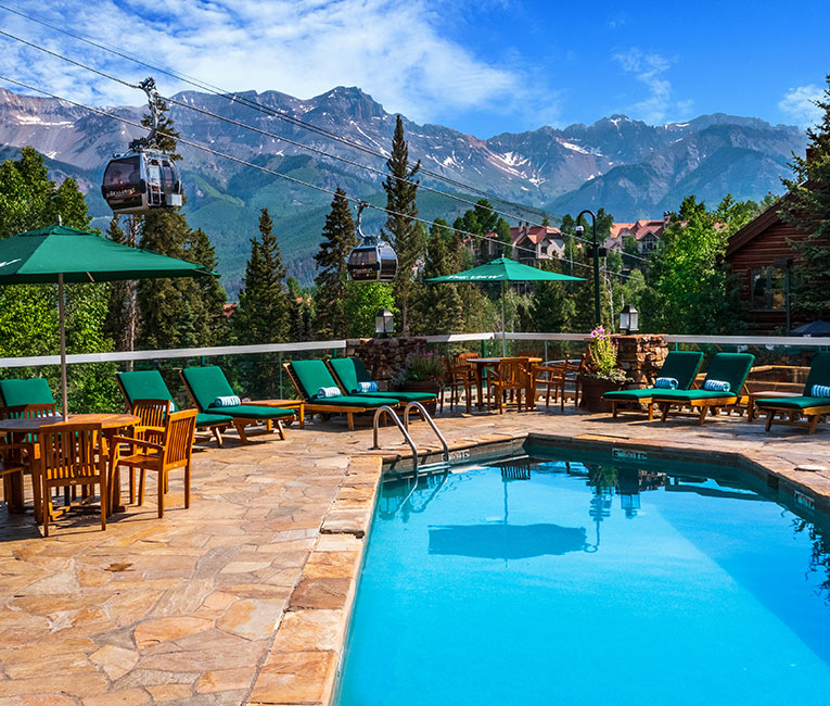 a blue pool and green lounge chairs with many mountains in the distance