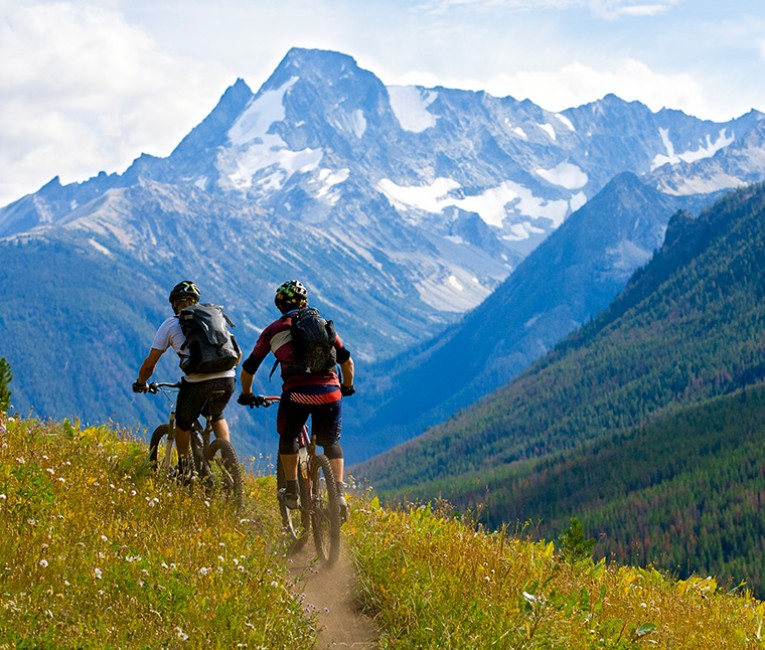 two people riding mountain bikes on a dirt path during the day