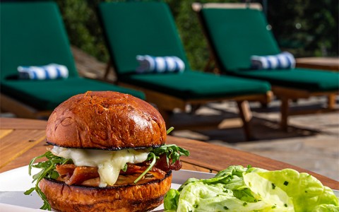 a sandwich with lettuce served on the side and pool loungers just behind it
