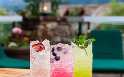 three colorful cocktails on a table near the pool with mountains in the distance