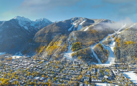 aerial view of homes and green trees with mountains covered lightly in snow