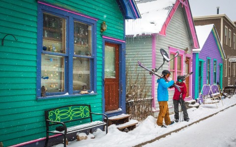 two skiers holding their skis in front of small colorful buildings