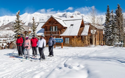 a group of skiers in front of a log building with snow all around them during the day