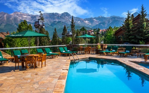 an outdoor pool and deck with green lounge chairs and the mountains in the distance