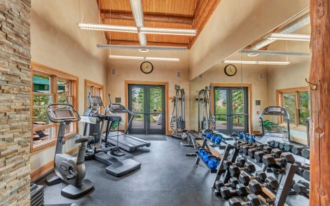a fitness room with a variety of workout equipment and lots of natural light from outside