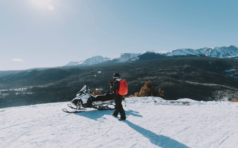 a person walking toward their snowmobile during the day with clear blue skies